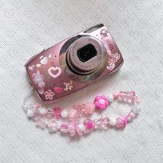 a pink camera sitting on top of a table next to a beaded necklace and lanyard