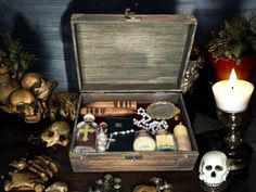 a wooden box filled with items on top of a table next to candles and skulls