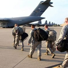 several soldiers are walking towards an airplane on the tarmac with backpacks in their hands