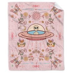 a pink blanket with an alien floating in the sky and flowers around it, on top of