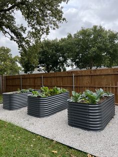 three metal planters with plants in them on the side of a road next to a fence