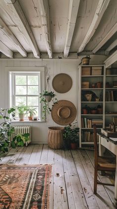 a room with white walls and wooden floors has plants on the floor, bookshelves, and a rug