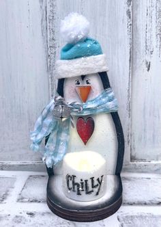 a snowman penguin with a blue hat and scarf holding a lit candle in front of a white door