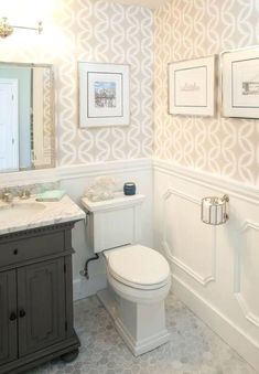 a white toilet sitting next to a sink in a bathroom under a mirror and framed pictures on the wall