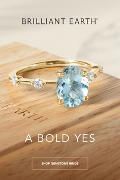 a ring with an aqua blue topazte and three diamonds on it, sitting on a wooden surface