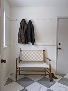 a bench and coat rack in the corner of a room with checkered flooring