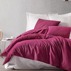 a bed with pink sheets and pillows in a room next to a chair on the floor