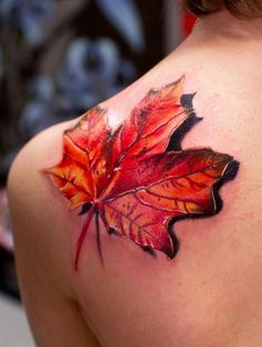 a leaf tattoo on the back of a woman's left shoulder, with red and orange leaves