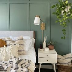 a bedroom with green walls, white bedding and plants on the nightstand next to it