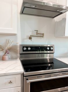 a stove top oven sitting inside of a kitchen next to white cupboards and drawers