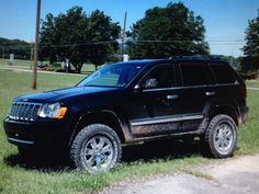 a black jeep parked on the side of a road in front of some trees and grass