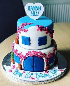 a three tiered cake decorated with flowers and blue doors is on a wooden table