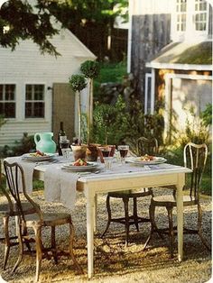 an outdoor table set for two with plates and glasses on it in front of a house