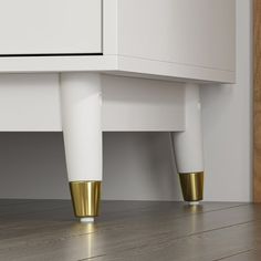 the legs of a white cabinet with gold accents on it and wood flooring underneath