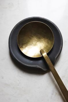 a metal spoon sitting on top of a white counter next to a black plate with a gold spoon in it