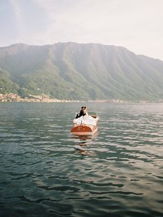 a person in a small boat on the water with mountains in the backgroud