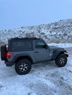 a gray jeep parked on the side of a road covered in snow with mountains in the background