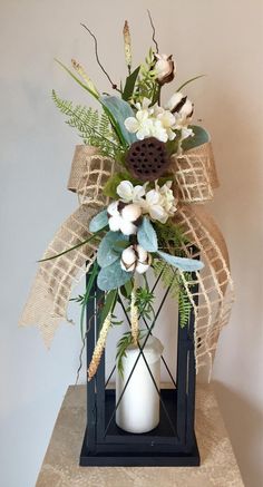 a vase filled with flowers and greenery sitting on top of a wooden table next to a wall