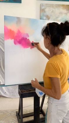 a woman in yellow shirt painting on easel