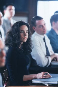 a woman sitting at a table in front of a laptop computer with other people behind her