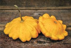 two small yellow pumpkins sitting on top of a wooden table