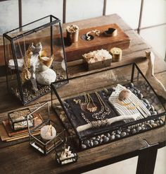 two glass boxes filled with jewelry sitting on top of a wooden table next to other items