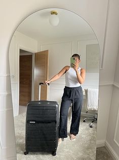 a woman taking a selfie in front of a mirror with her suitcase and cell phone