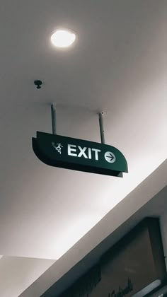 an exit sign hanging from the ceiling in a room with white walls and lights above it