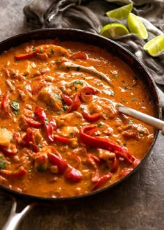 a skillet filled with curry and red peppers on top of a table next to limes