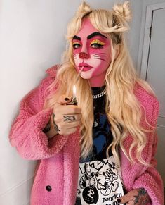 a woman with pink makeup holding a lit candle in her hand while wearing a cat costume