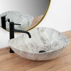 a marble bowl sink sitting on top of a wooden floor next to a round mirror