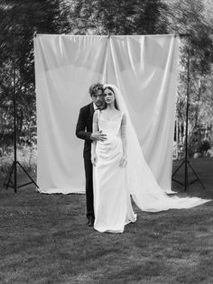 a man and woman standing next to each other in front of a white curtain on the grass