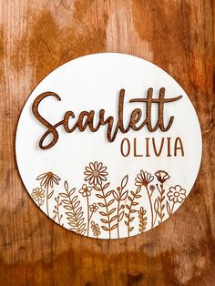 a wooden sign with flowers on it that says scarlettet oliva in brown lettering