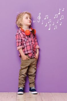 a little boy standing in front of a purple wall with musical notes on it's side