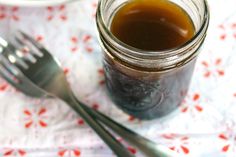 a spoon and fork sit next to a jar of liquid on a tablecloth with red flowers