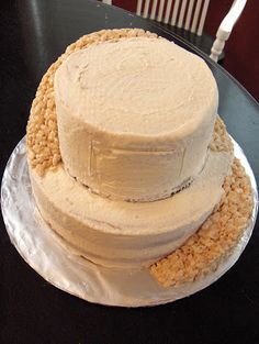 three tiered cake sitting on top of a black table next to a white chair