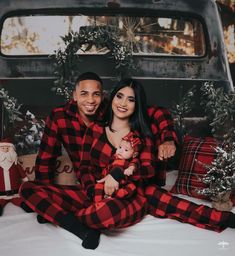 a man and woman in plaid pajamas sitting on a bed with christmas decorations around them