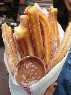 a person holding a basket filled with churros and dipping sauce