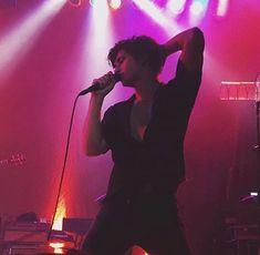 a woman singing into a microphone while standing in front of a stage with bright lights