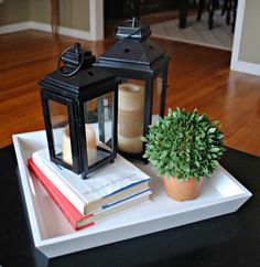 a candle and some books on a tray with a potted plant in the middle