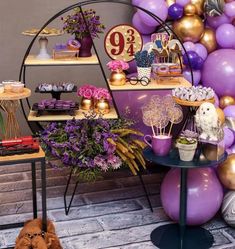 a table topped with lots of purple balloons next to a shelf filled with cakes and desserts