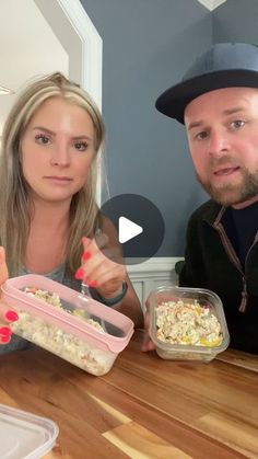 a man and woman sitting at a table with food in plastic containers on their hands