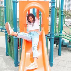 a woman sitting on top of a slide in a playground