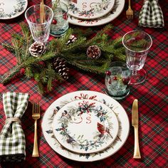 the table is set for christmas dinner with pine cones, evergreen branches and plaid napkins