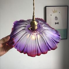 a hand holding a purple flower shaped light fixture in front of a painting on the wall