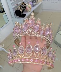 a hand holding a pink and gold tiara in front of a store display case