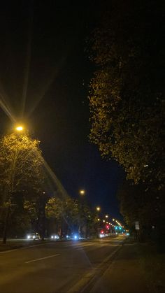 an empty street at night with the lights on and trees in the foreground lit up