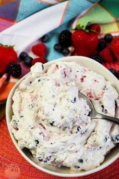 a bowl filled with ice cream next to berries and strawberries on a colorful table cloth