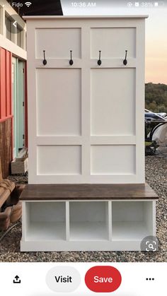 a white wooden bench sitting in front of a red and white building with hooks on it's doors