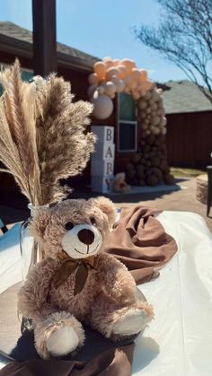 a brown teddy bear sitting on top of a table next to a vase filled with dry grass